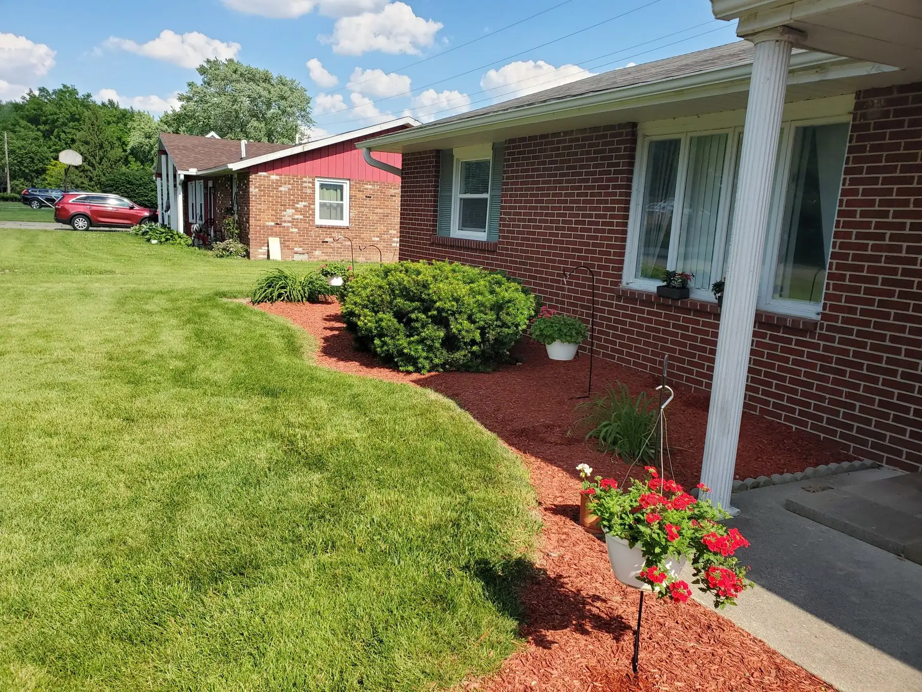 Freshly edged bed with red mulch and trimmed shrubs beside a brick home, lawn cut clean